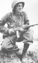 Soldier with rifle, kneeling in field during Korean War.